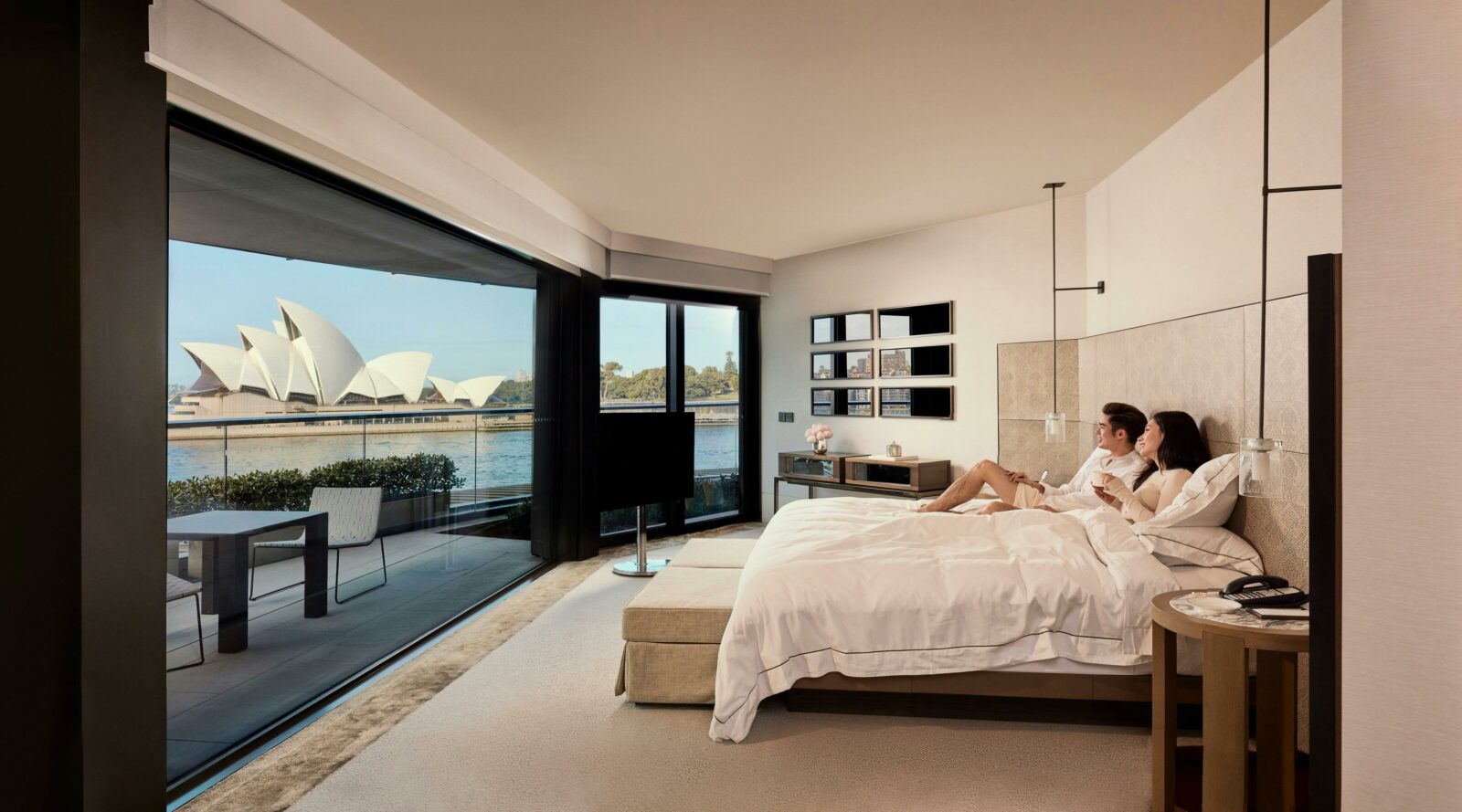 Couple enjoying the spectacular views of Sydney Harbour from their bedroom at the Park Hyatt
