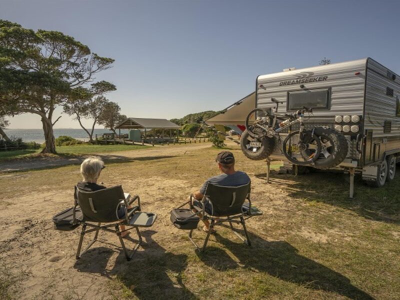2 people sitting down beside their campervan looking out at the ocean at Point Plomer campground,