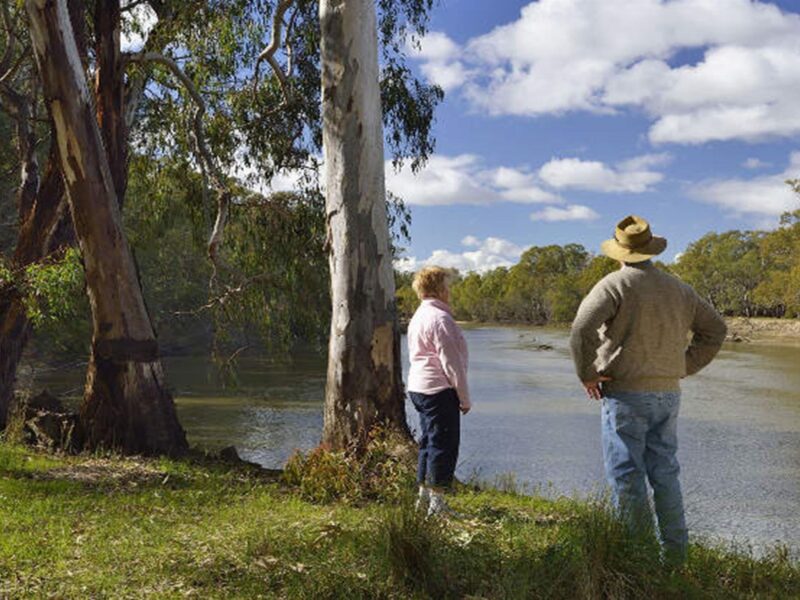 View of the Murrumbidgee River, with a woman and man in the foreground standing on the river bank.