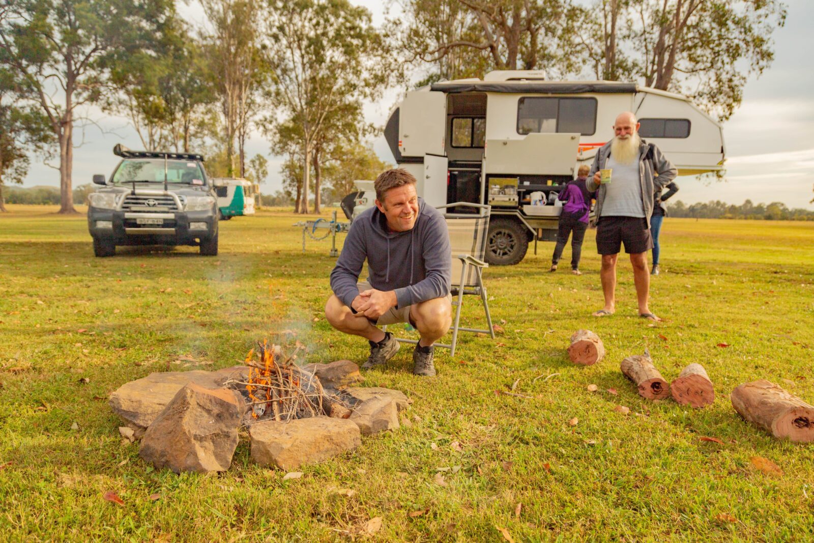 Man sitting around fire with caravan in background