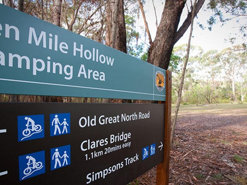 A visitor enters Ten Mile Hollow campground behind a sign for the campground in Dharug National Park