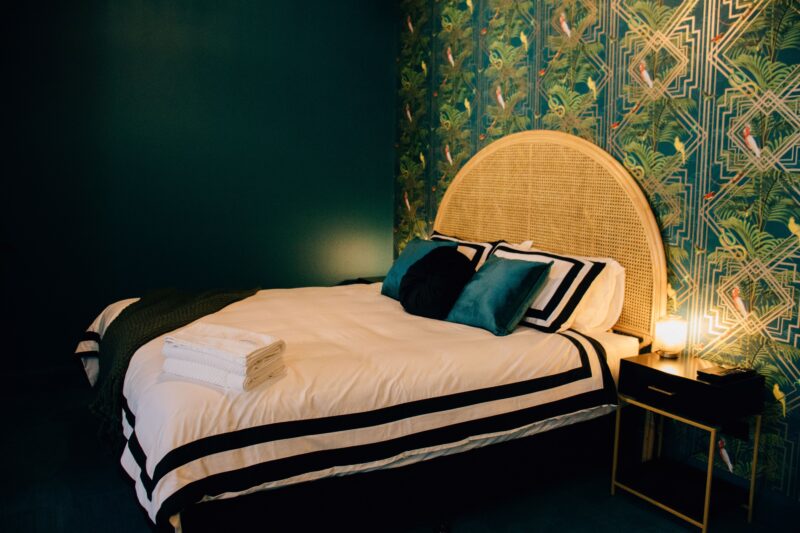 A King size bed set against bold teal art deco wallpaper.