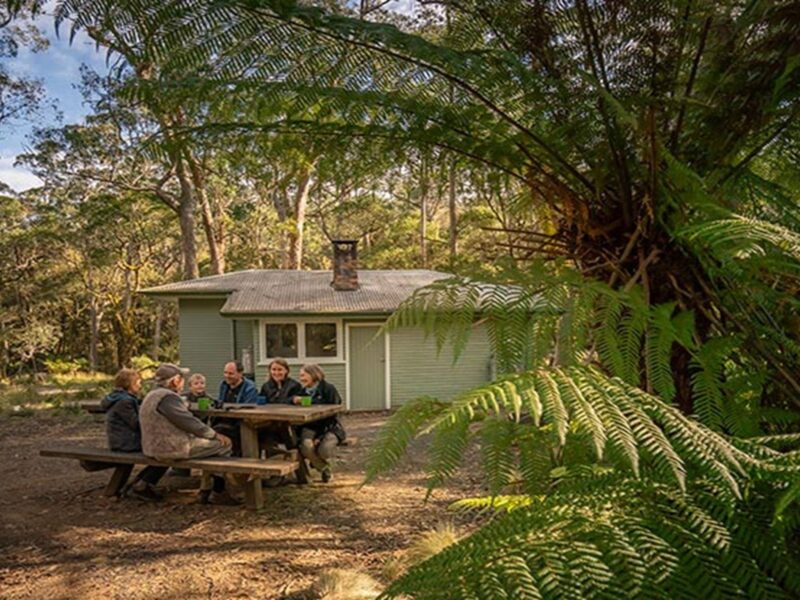 Family sitting around the picnic table outside Toms Cabin. Photo: John Spencer © DPIE