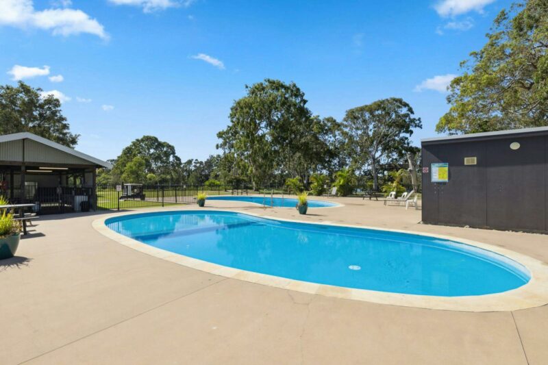 Image of 2 kidney shapped pools. Large gum trees agains a blue sky in the background.