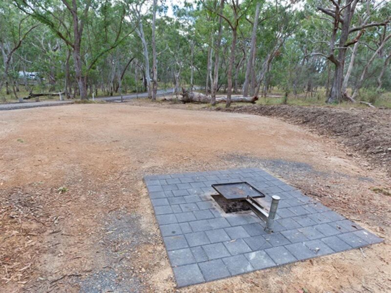 Campsite with an open fire pit with a swivelling BBQ plate over the top, Wollomombi campground,