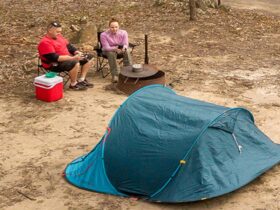2 campers sitting next to a fire pit barbecue behind their tent. Photo: John Spencer/DPIE