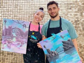 couple holding their paintings of the sydney skyline at a paint and sip session in sydney