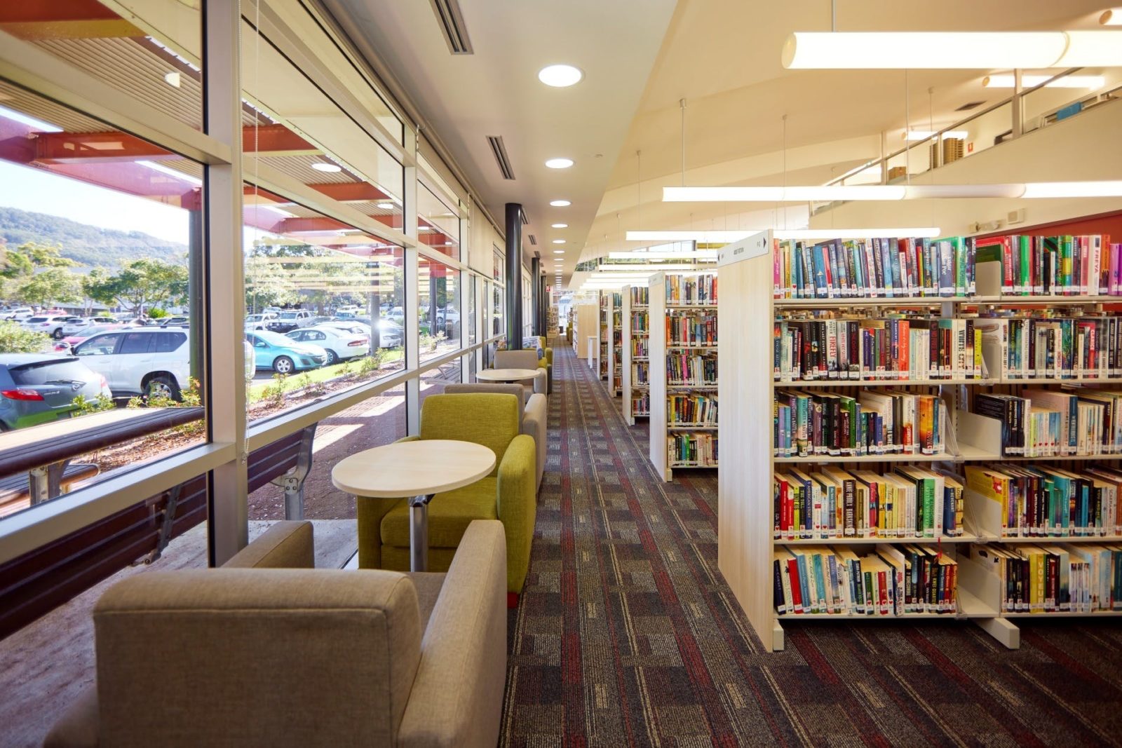 Comfortable lounge chairs and small tables adjacent to large windows and book shelves.