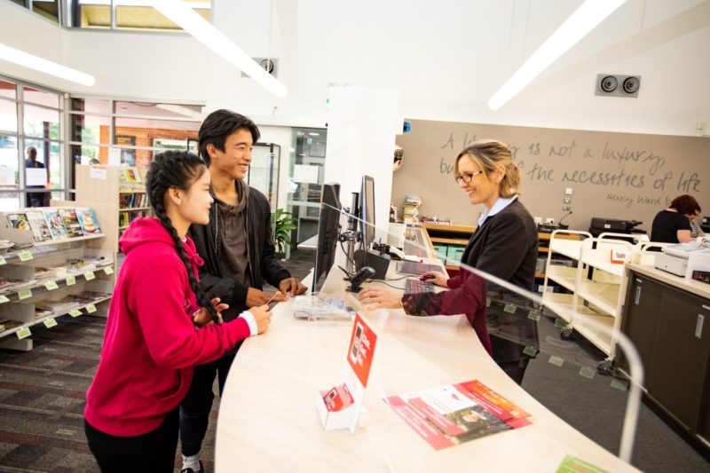 A librarian assisting two young customers at the service desk.