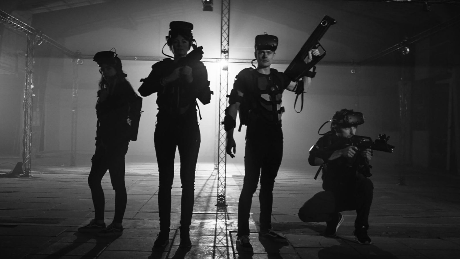 Four people holding guns wearing virtual reality equipment