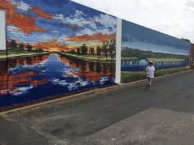 Two scenes of the Murray River painted on a brick wall. One is a sunset and the other is blue sky.