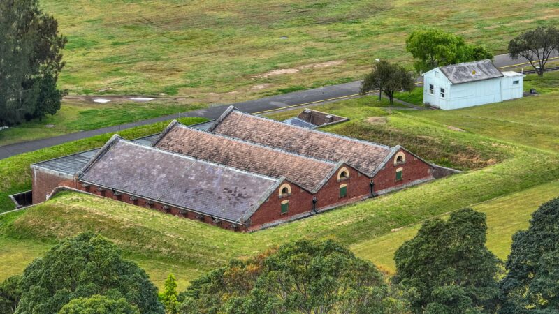 Birds eye, drone view of red brick heritage building with 3 gable roofline, surrounded by grass.