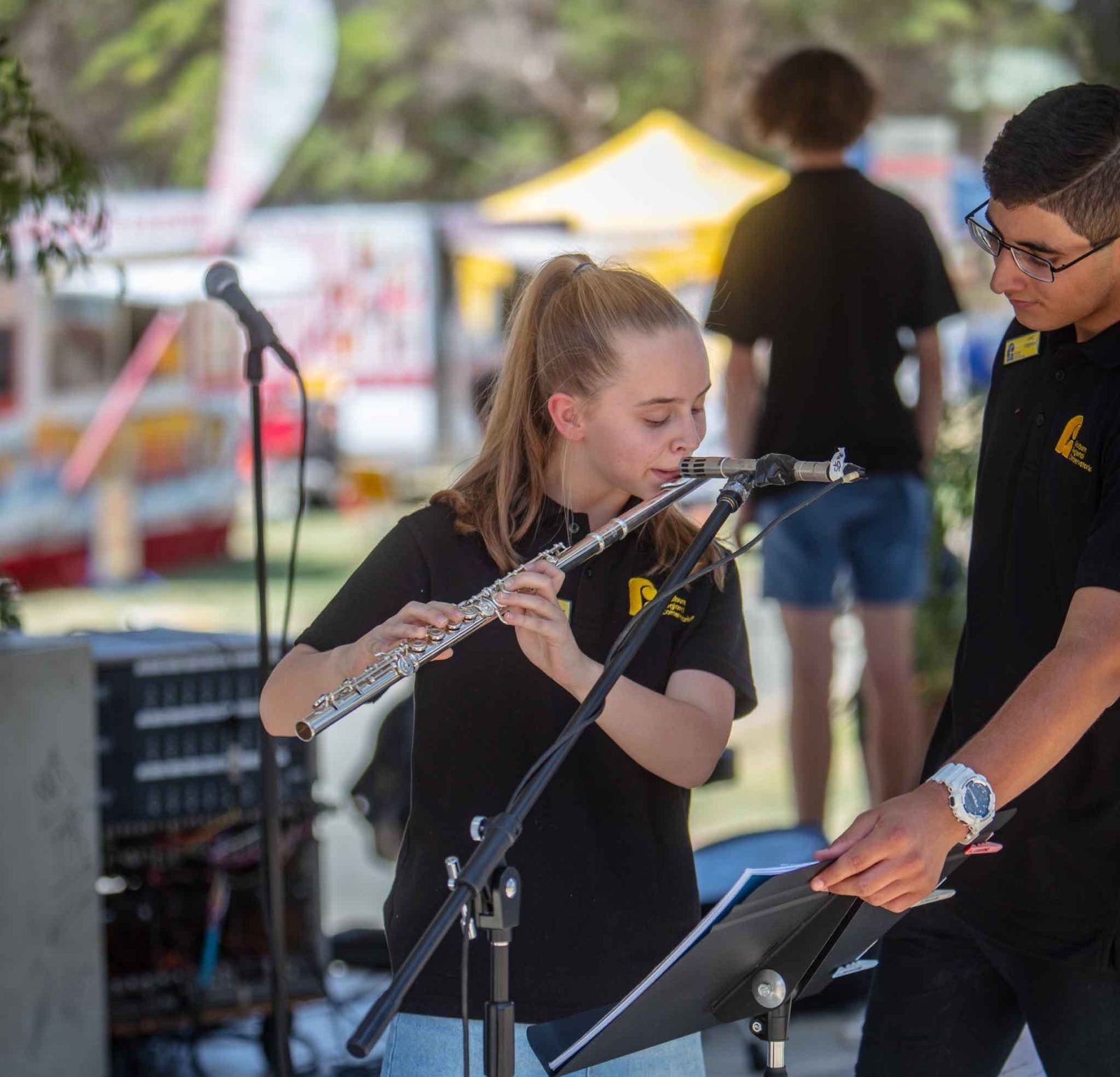 A young girl playing the flute whilst on stage with young man turning the music pages