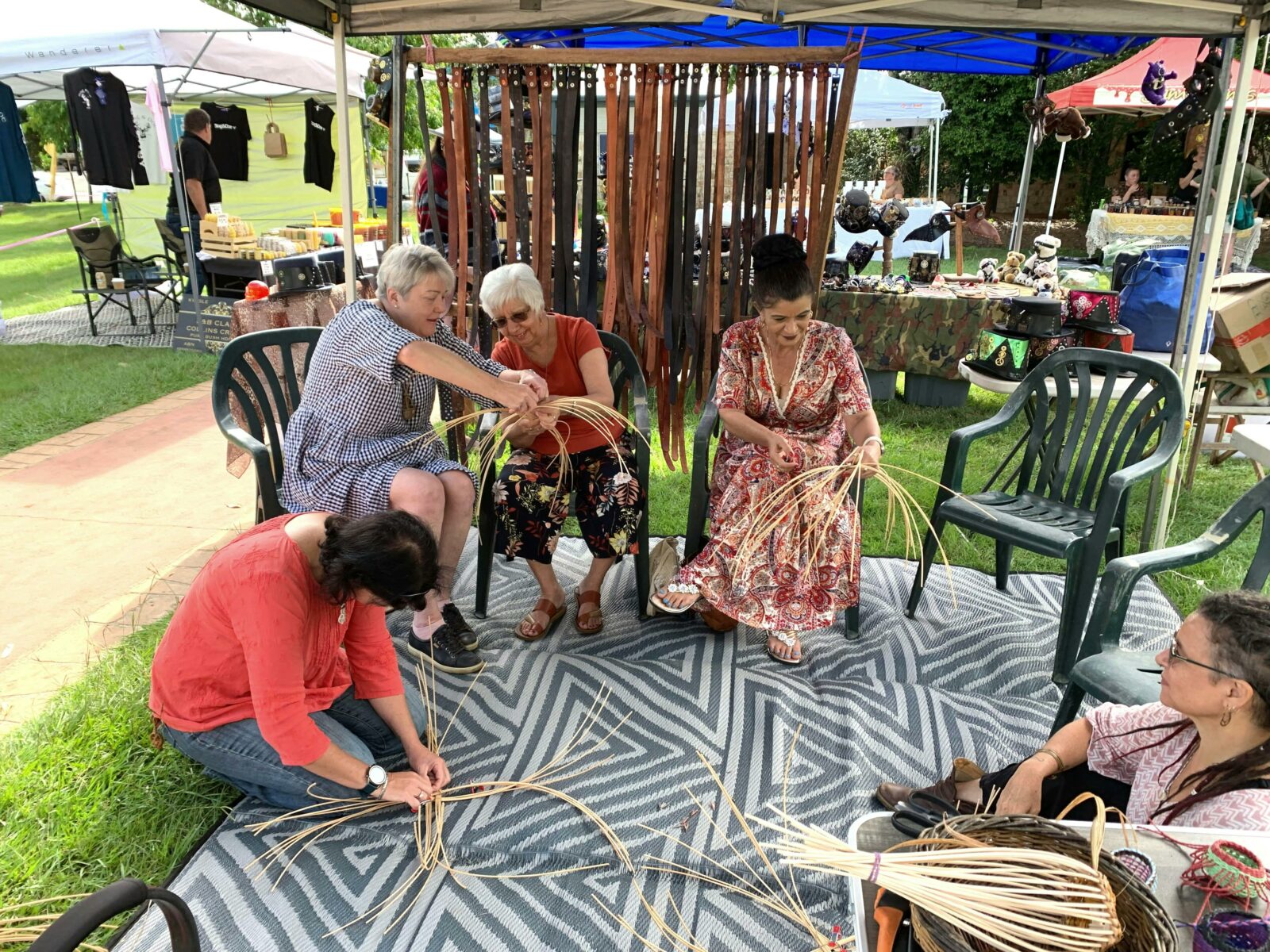 Four ladies weaving a part made basket and getting help.