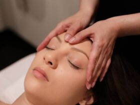 A lady getting a spa facial treatment with her eyes closed and two hands massaging her forehead