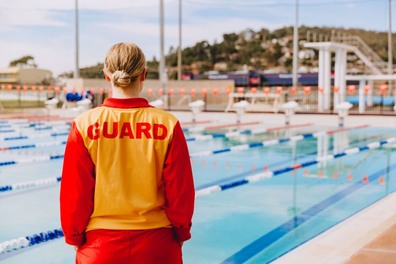 A life guard in uniform watches over the outdoor olympic pool