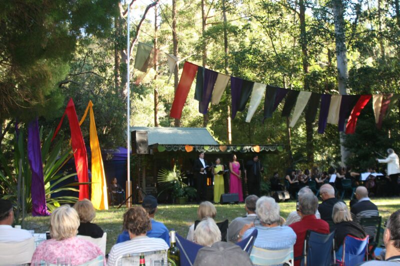 A musical event at the Arboretum. Colourful flags flying above the audience.