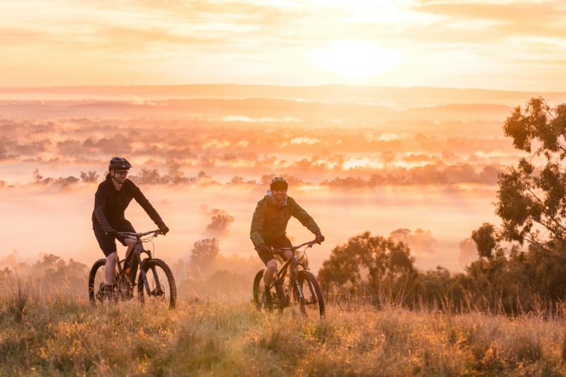 Two cyclist at the peak of a reserve during a glowing sunrise