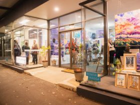 An angled photograph from the street of multiple shopfront windows filled with artworks.