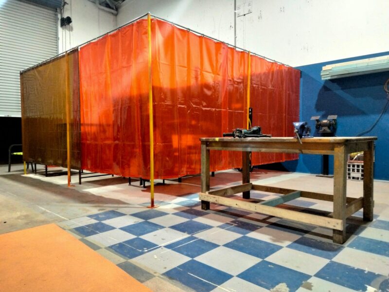 A warehouse with blue and white checkered floor with an orange and red welding curtain area