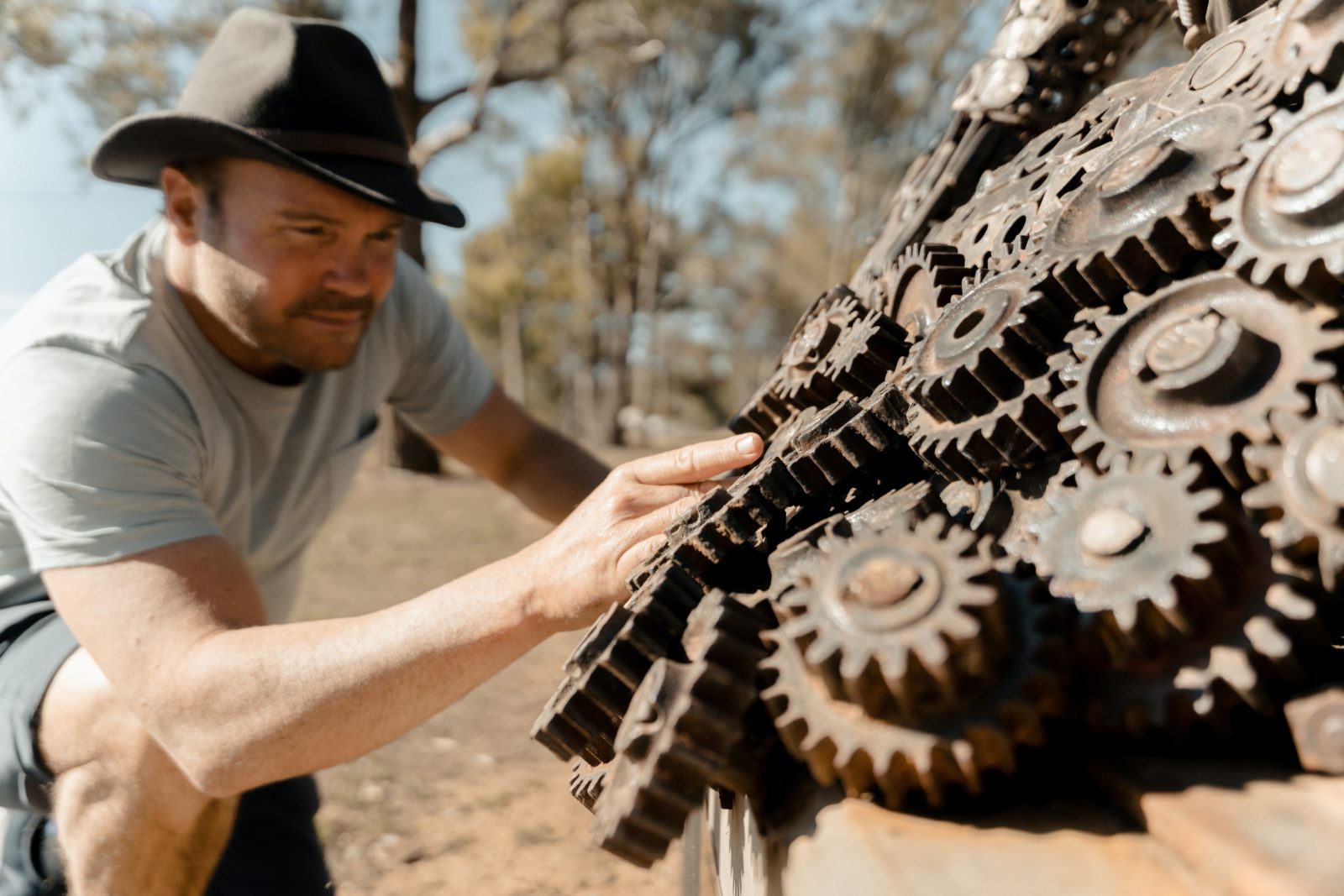 A man rests a hand on iron cogs that form the fleece of a ram sculpture.