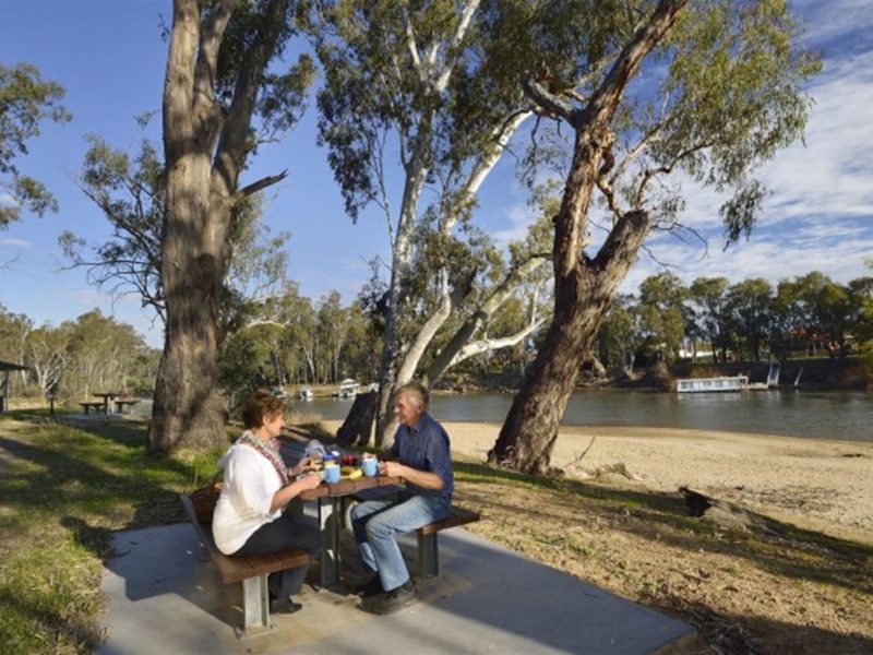Two people at a picnic table at Ski Beach picnic area next to Murray River in Murray Valley Regional
