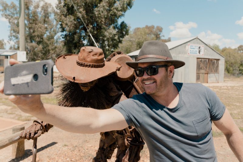 A man takes a selfie with the scrap metal swagman sculpture.