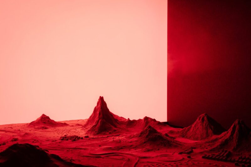 An artwork of a sci-fi landscape made out of sand and wood with a red light backdrop
