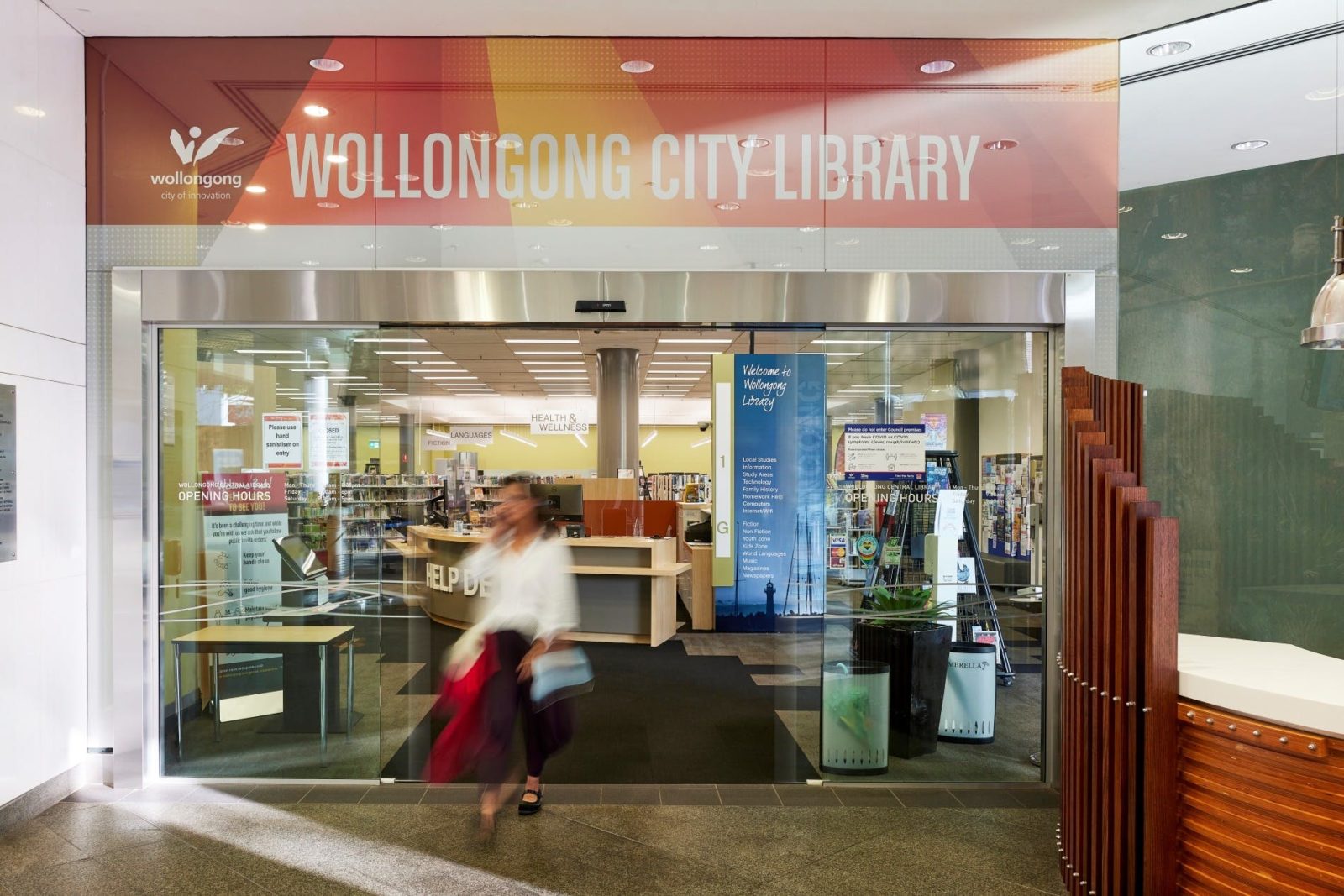 A woman walking out of the Wollongong Library front doors into a foyer.