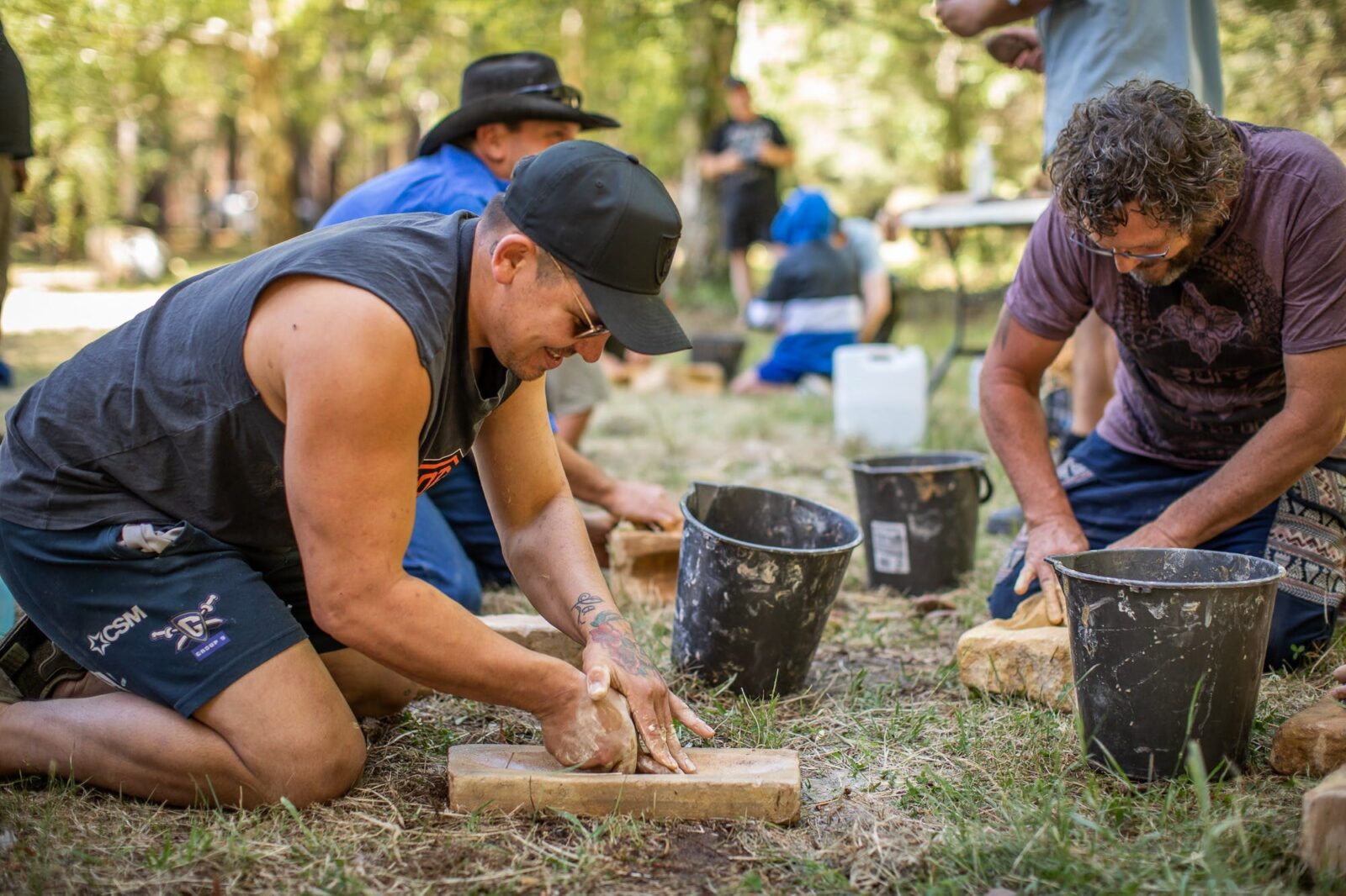 Men grinding stone to make a traditional Aboriginal axe head in a workshop