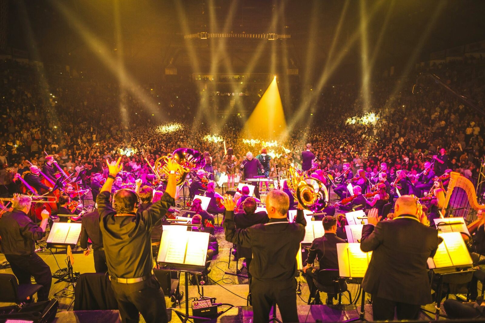 An orchestra performs to a crowd, with bright flashing lights overhead