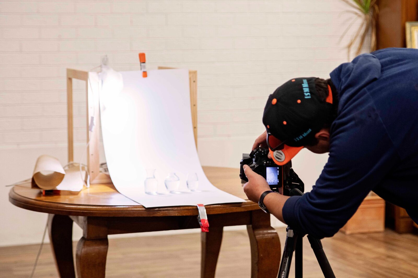 a person with a camera on a tripod taking a photo of 3 small vases on a white backdrop.