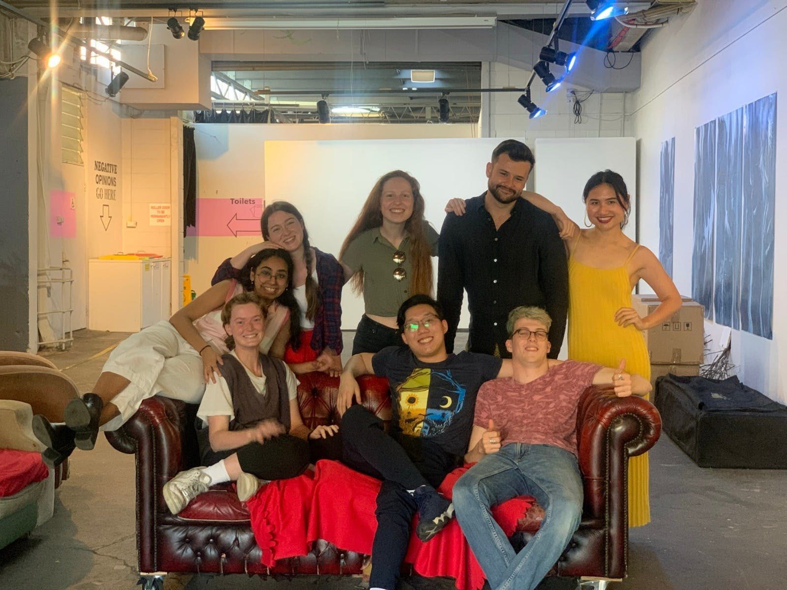 Eight Young People sit smiling together on a lounge in 107 Projects Art Space.
