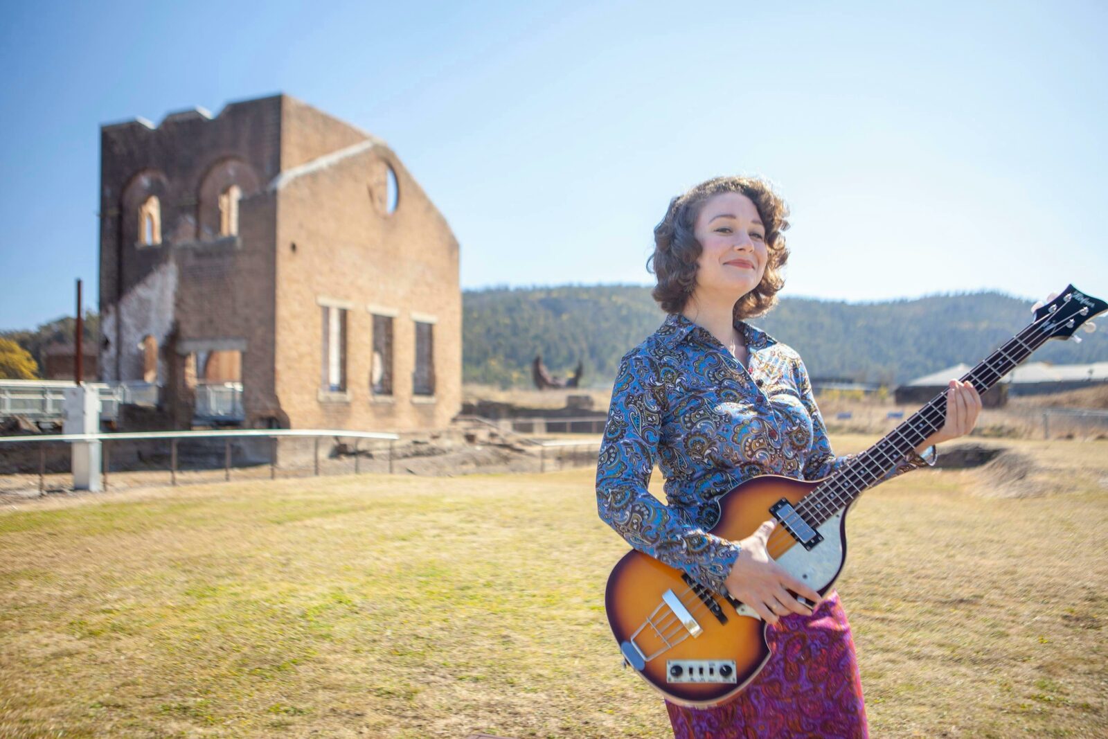 Woman playing Hofner bass in front of Lithgow blast furnace