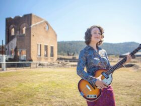 Woman playing Hofner bass in front of Lithgow blast furnace