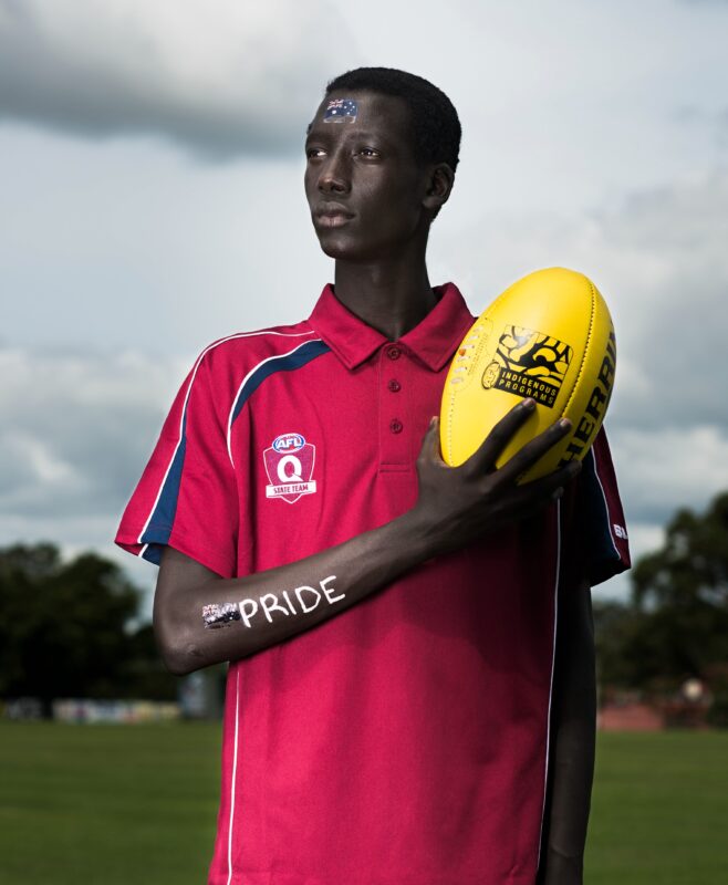 photo shows a young male refugee holding an australian rules football