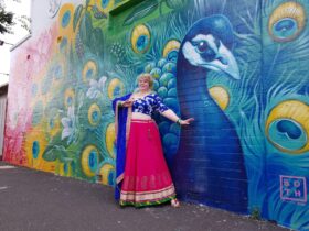A women dressed in Bollywood attire posting in front of a large mural of a peacock