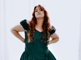 Red-haired woman in green dress, confidently posing with hands on hips.