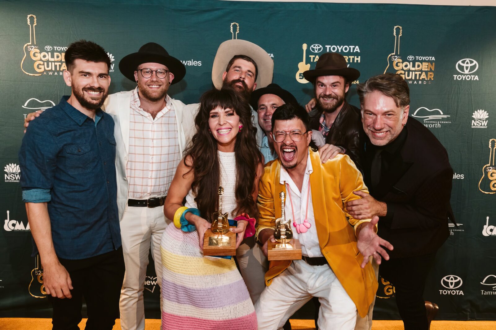 Female artist holding a golden guitar trophy surrounded by smiling male bandmates.