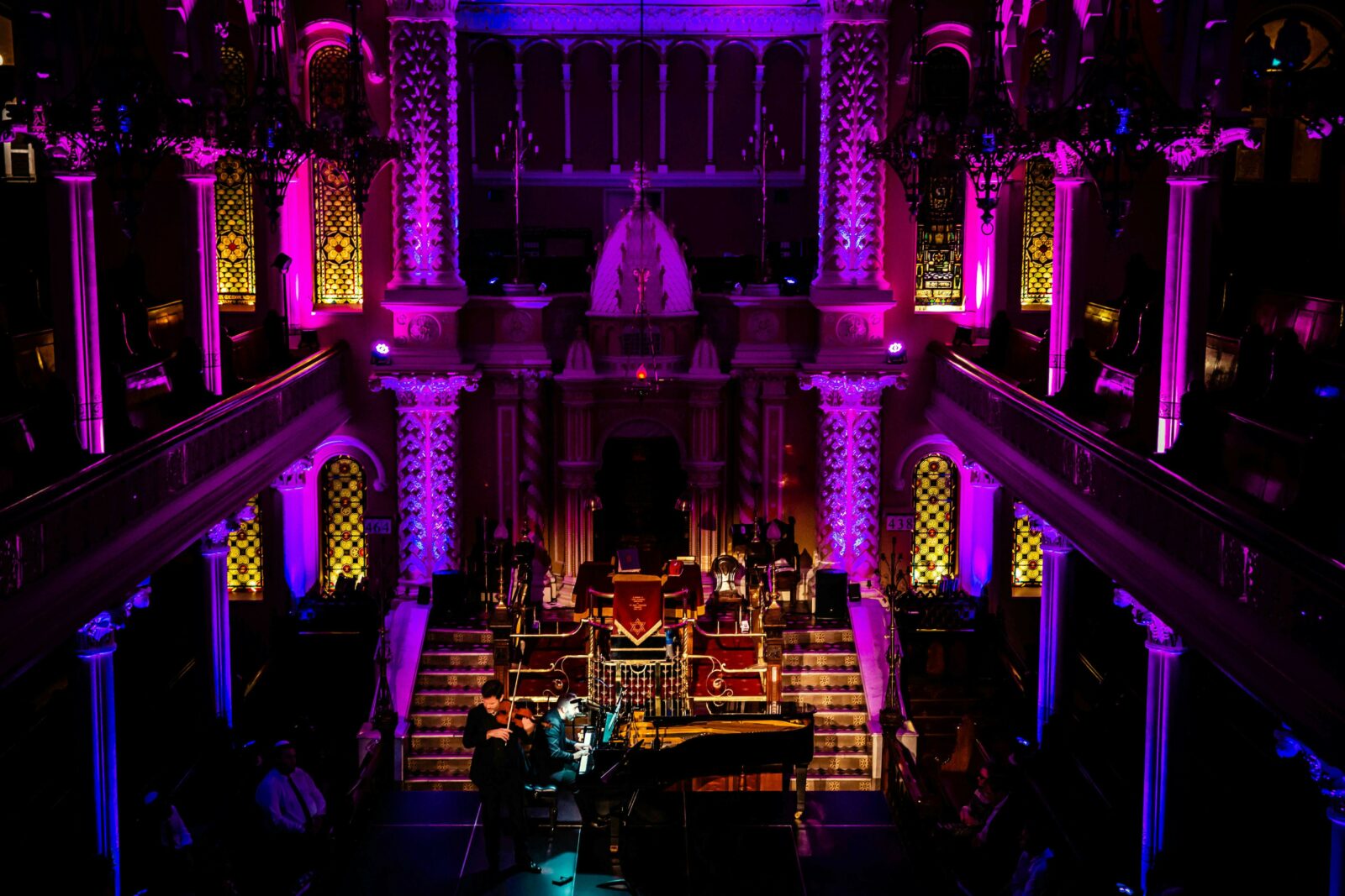 A concert at the great Synagogue with pink and purple lighting and a gran piano with a violinist