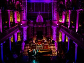A concert at the great Synagogue with pink and purple lighting and a gran piano with a violinist