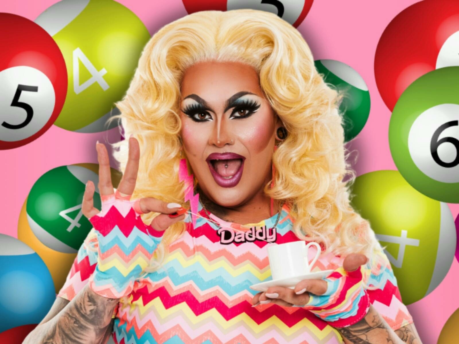 Drag performer wearing colourful striped clothes and with blonde hair and bingo balls in background