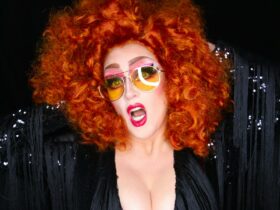 Bold Red Haired woman with sunglasses on and her mouth open with red lipstick