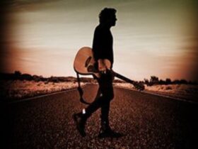 Ian Moss walking on the road, holding guitar