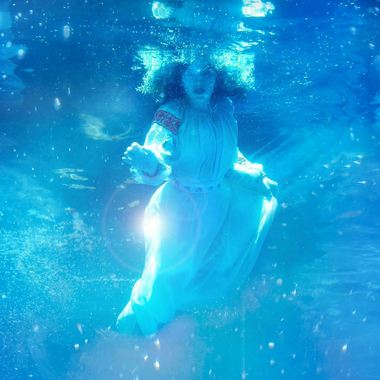 A girl in Ukrainian dress floats underwater, reaching forward