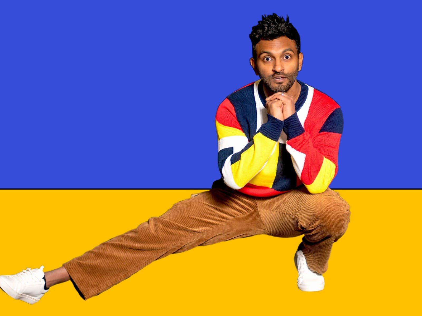 Man crouching with right leg extended out in front of blue and yellow backdrop