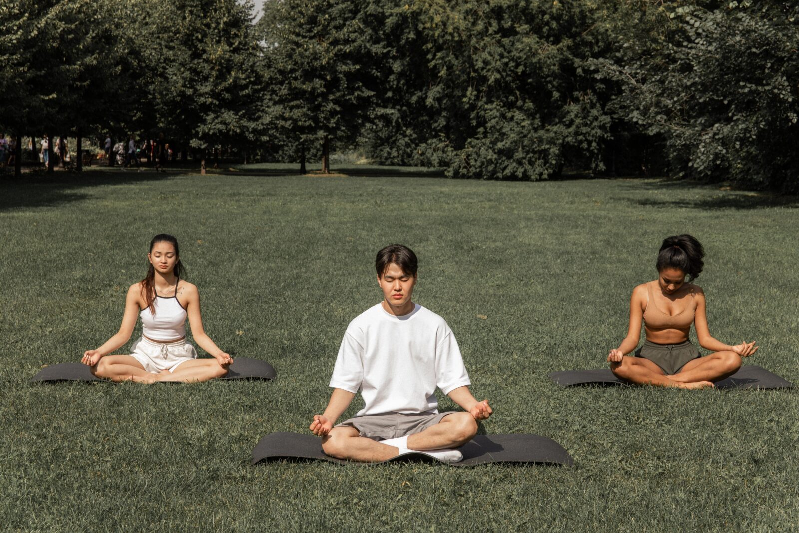 three individuals meditating on grass outside