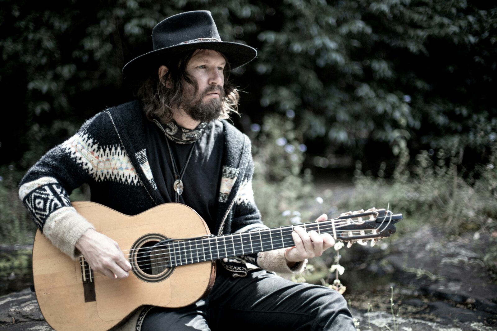Musician Paul A. George in traditional western attire, sporting a beard. playing a guitar.