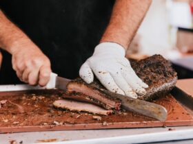 A hand holds a knife cutting ribs while the other hand stabilises the meat on a chopping board