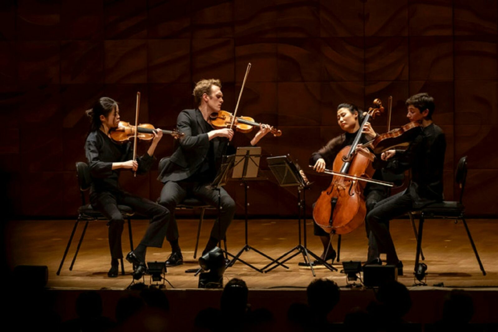 a string quartet, playing on a stage. All four musicians are dressed in black & lit by a spotlight